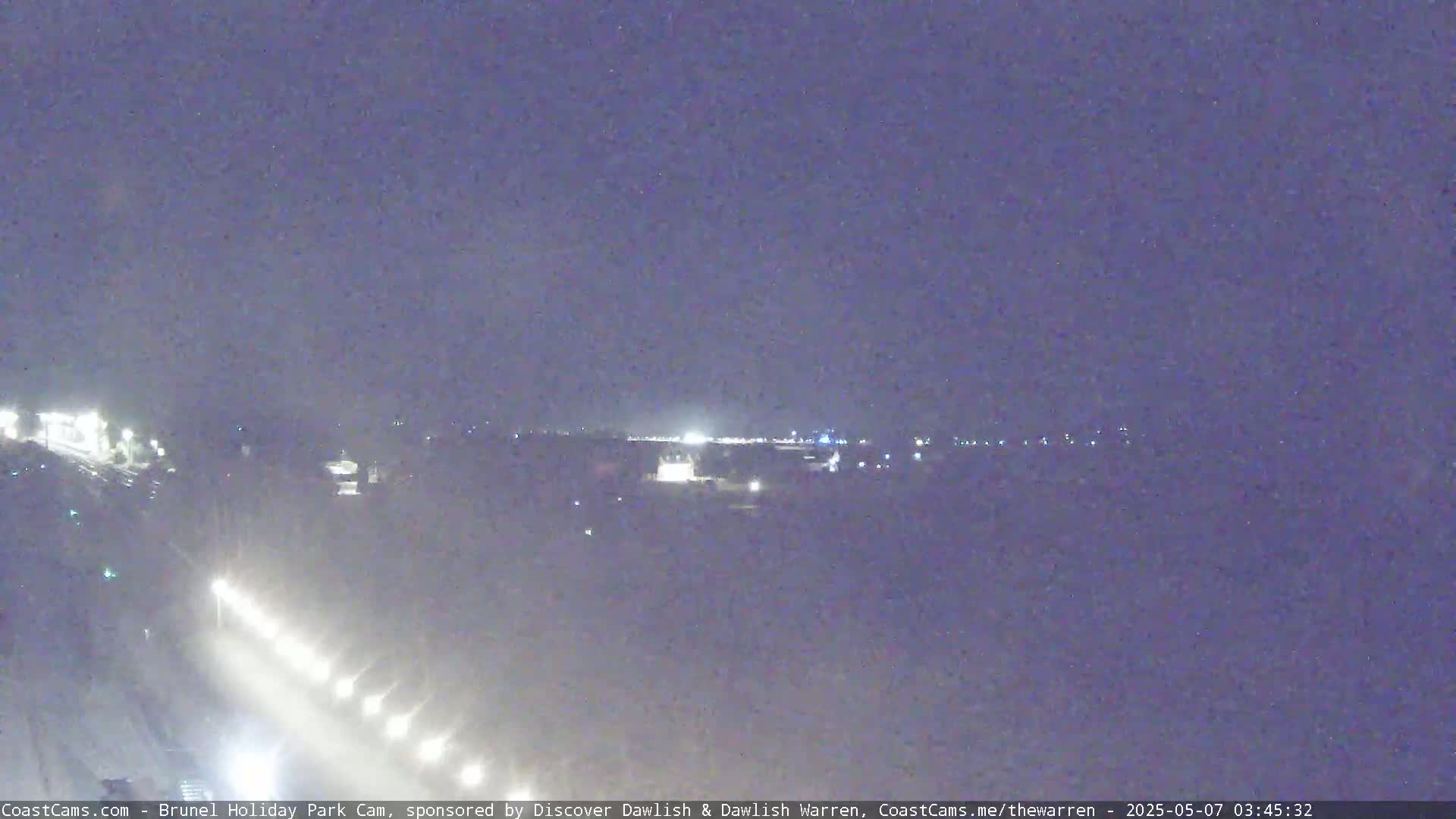 A nighttime long shot of a highway with a few cars visible, under a hazy, dark sky.