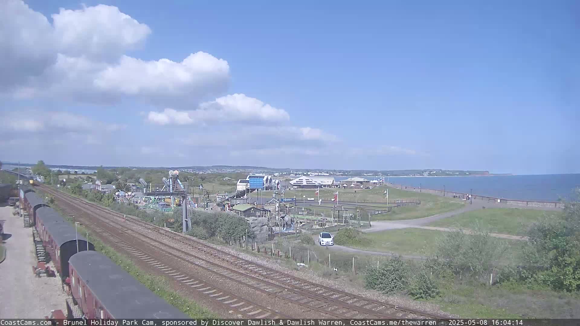 A seaside amusement park with a train track running through it, under a partly cloudy sky.