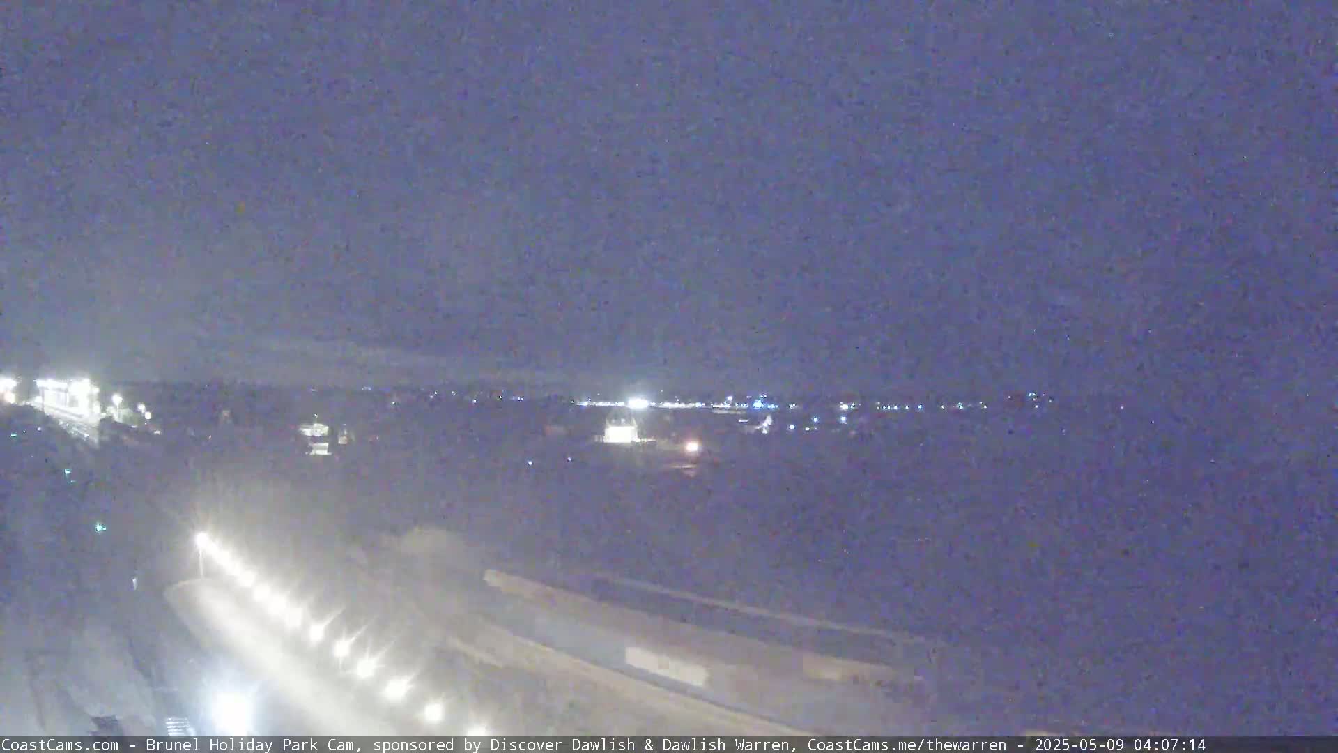 A nighttime view of a highway with traffic and a distant town illuminated under a dark, overcast sky.