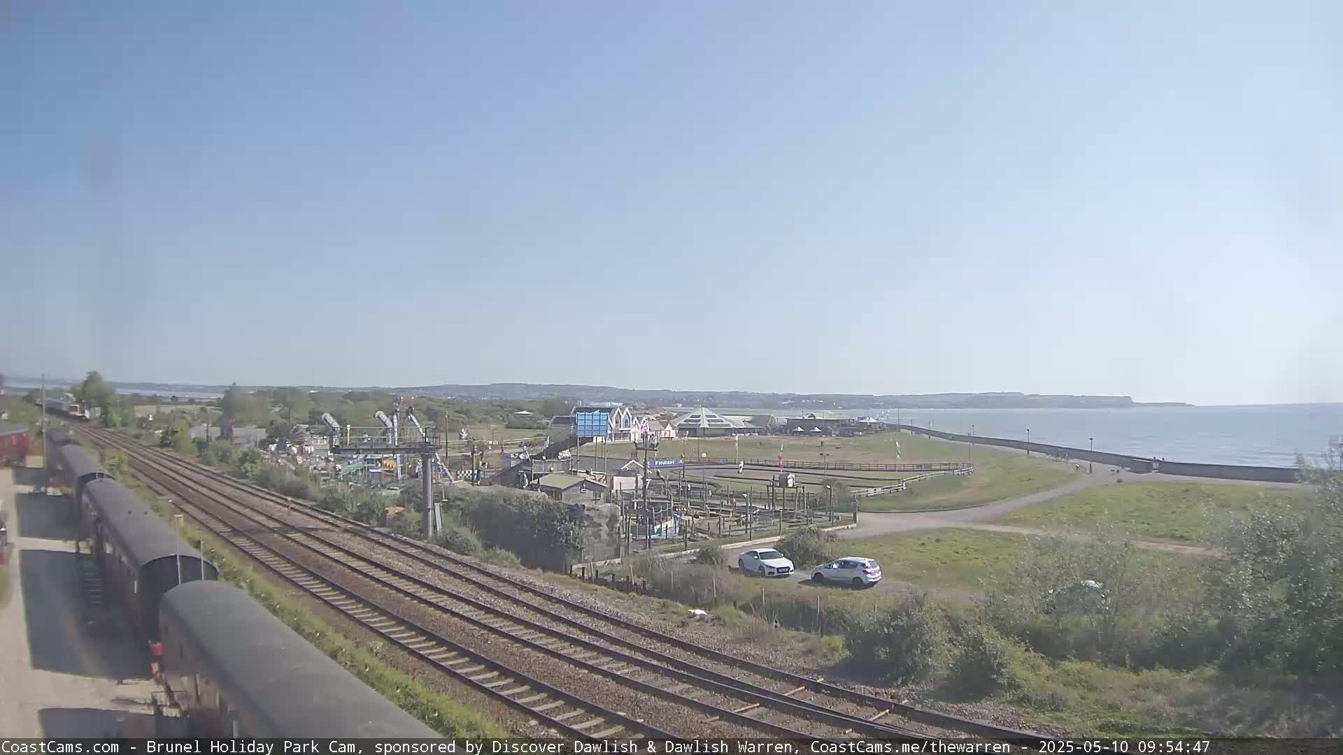 A sunny day shows a seaside amusement park next to train tracks and a calm ocean.