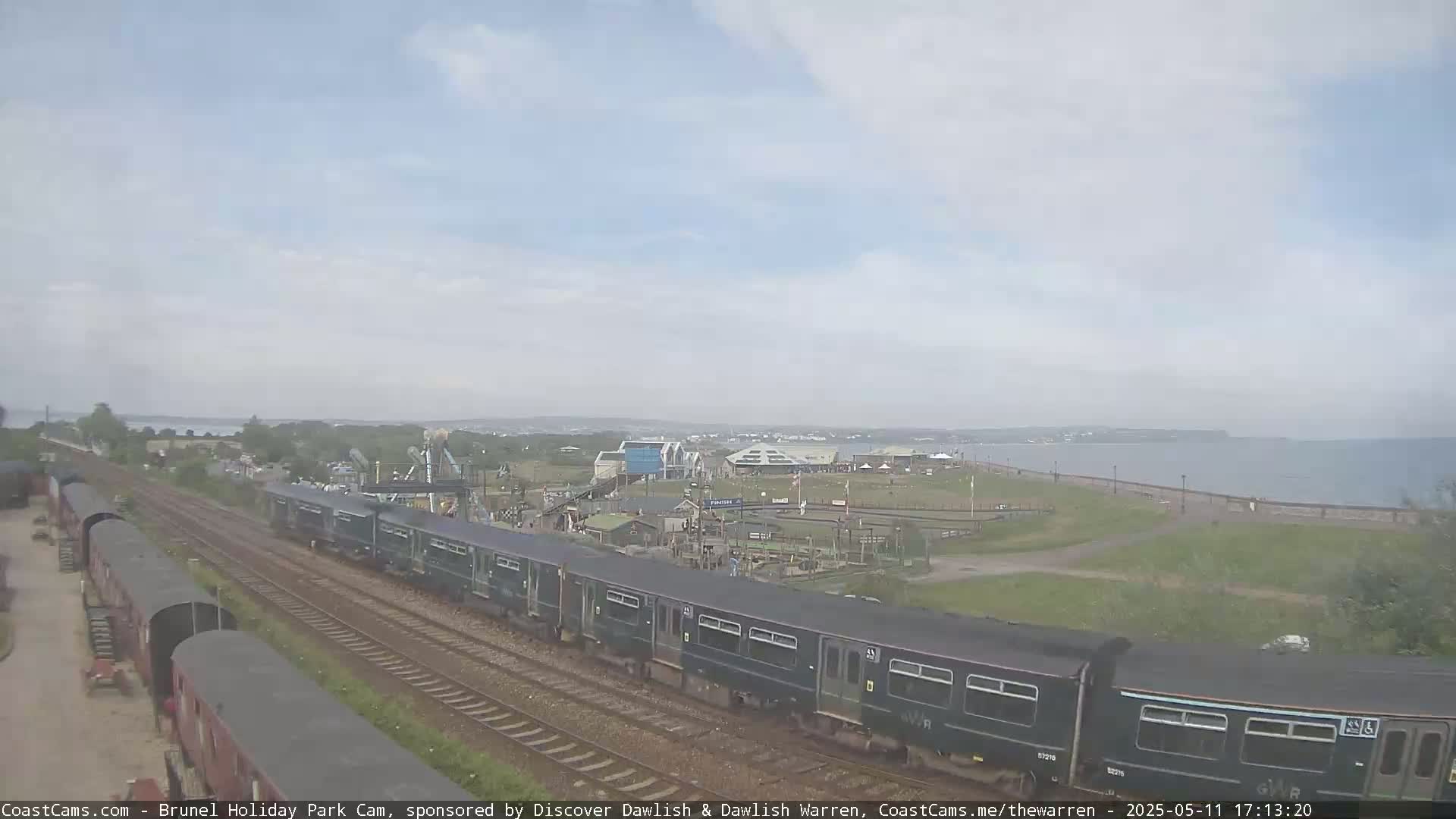 A long train passes by a seaside amusement park on an overcast day.