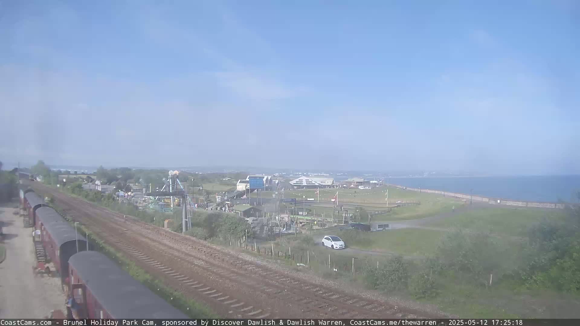 A seaside amusement park is visible from a vantage point overlooking train tracks on a partly cloudy day.
