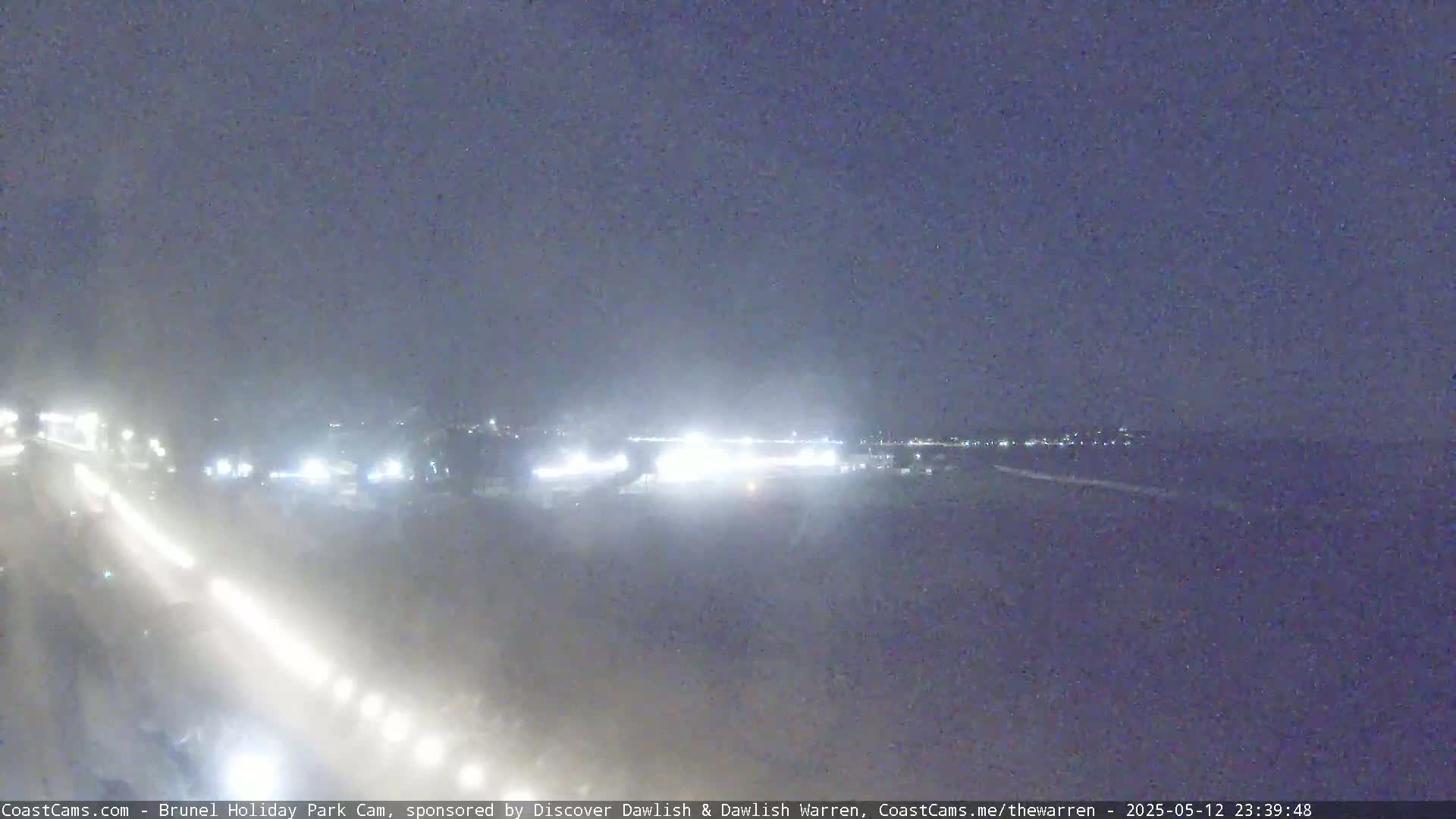 A nighttime view of a road with headlights and distant city lights under hazy conditions.