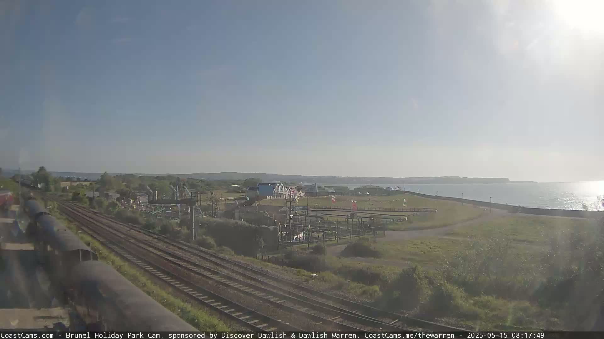 A sunny day overlooking a coastal amusement park with train tracks running nearby and a calm sea in the distance.