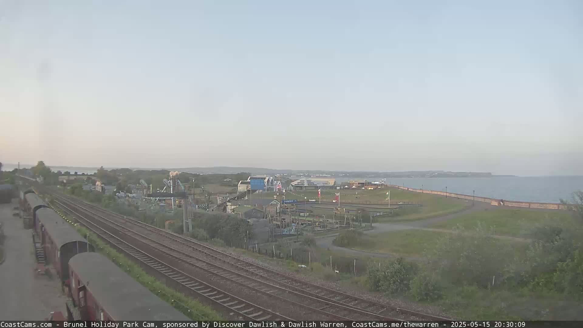 A seaside amusement park is visible beyond a railway line, under a hazy sky.
