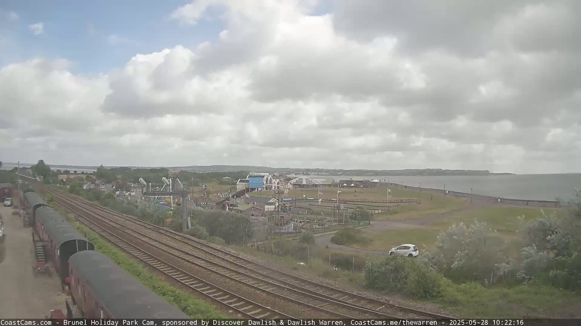 A cloudy day overlooks a coastal amusement park next to train tracks and a body of water.