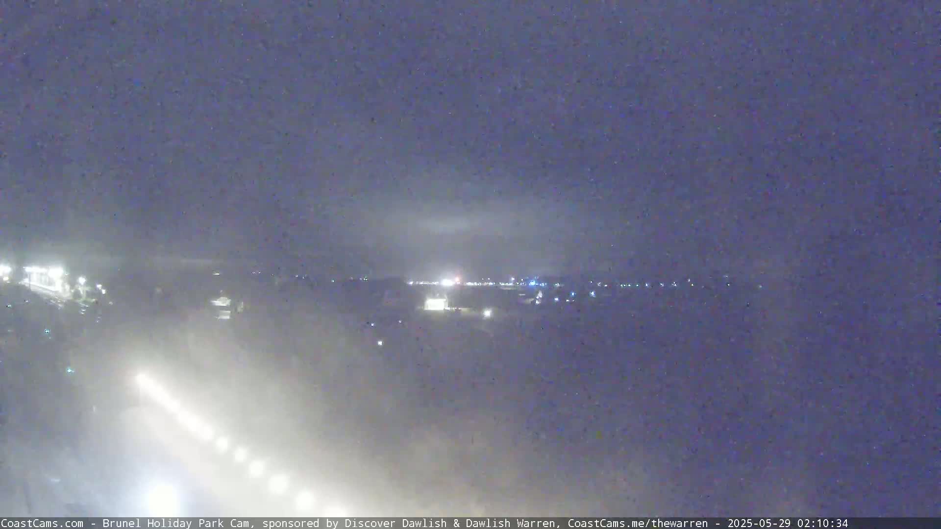 A hazy nighttime view shows distant lights in a town or city under a dark sky.