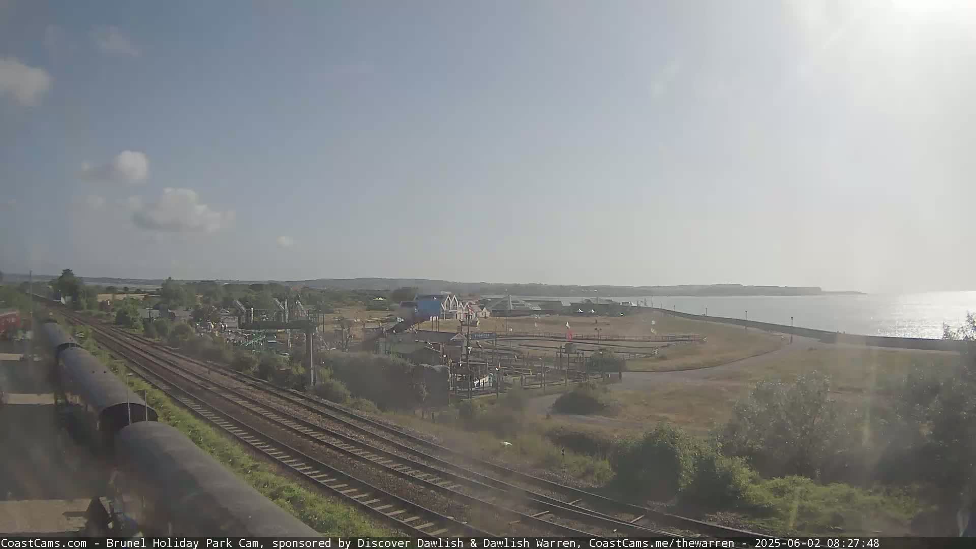 A sunny day reveals a seaside amusement park near a railway track and body of water.