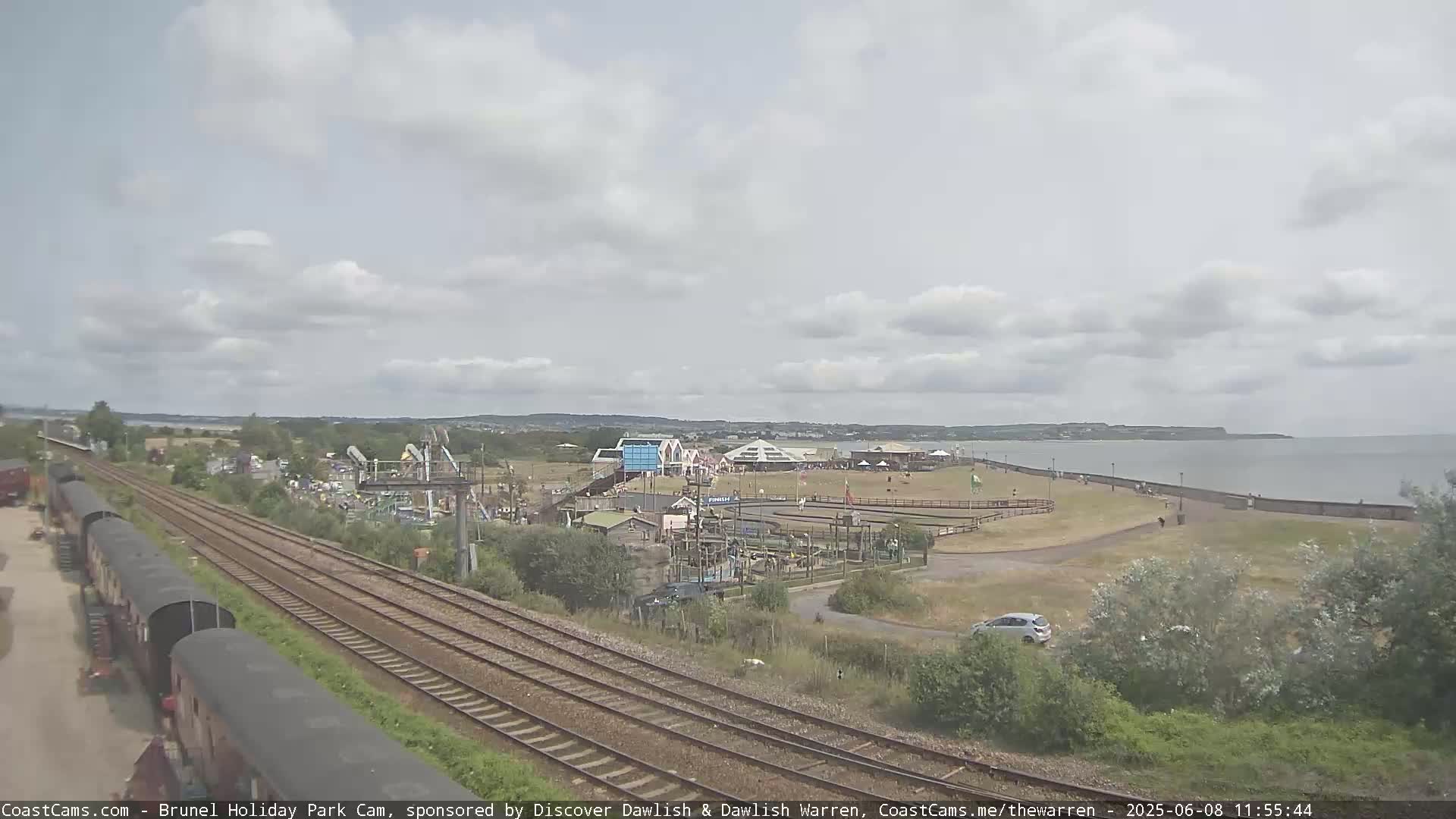 A seaside amusement park with a train track nearby, under a partly cloudy sky.