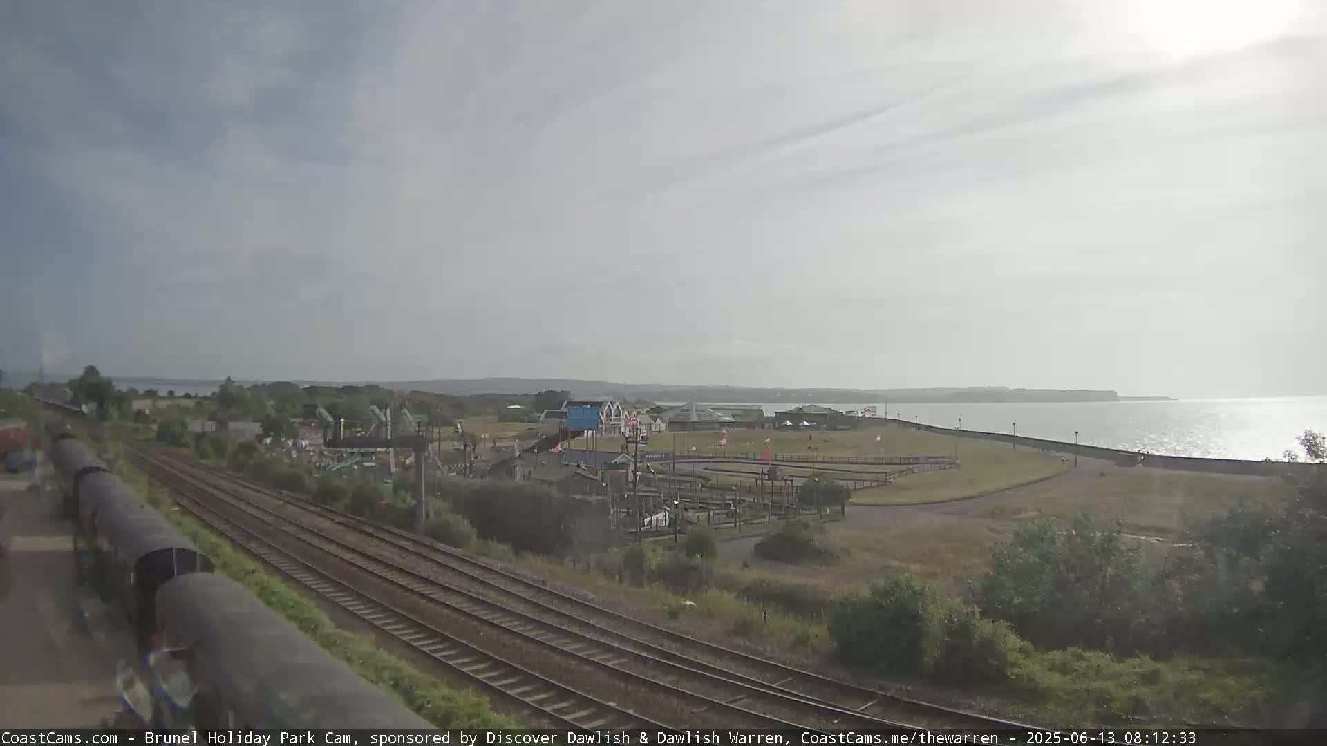 A seaside amusement park with a go-kart track and playground is visible near a railway line under an overcast sky.