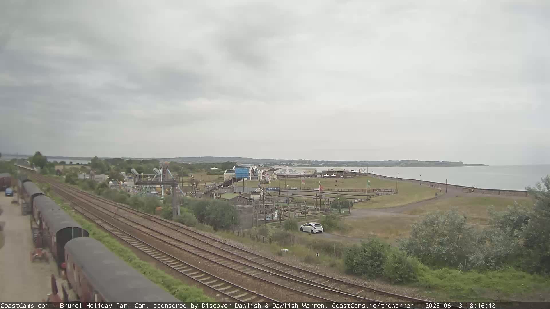 A seaside amusement park is visible beyond a set of train tracks on an overcast day.