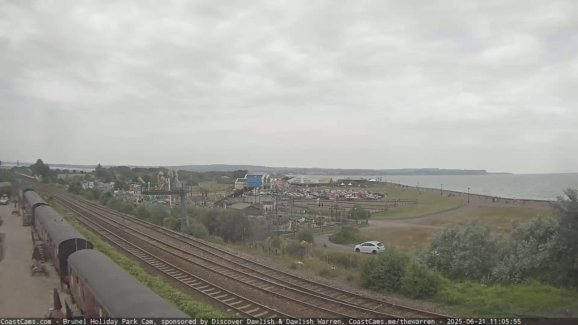 A seaside amusement park with a train track running alongside it is viewed on an overcast day.
