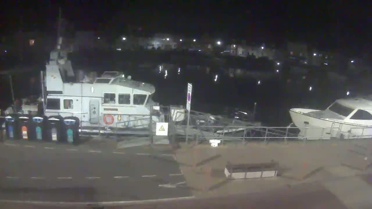 At night, a large white patrol boat is docked next to a smaller white motorboat at a harbor, under a clear, dark sky.