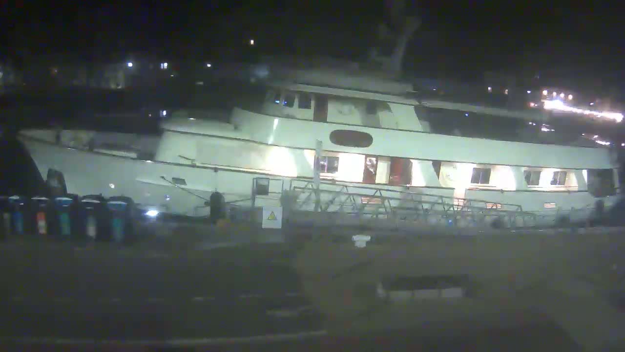 A large, light-colored motor yacht is docked at night.