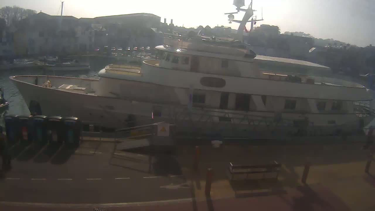A large motor yacht is docked at a marina on a hazy, sunny day.