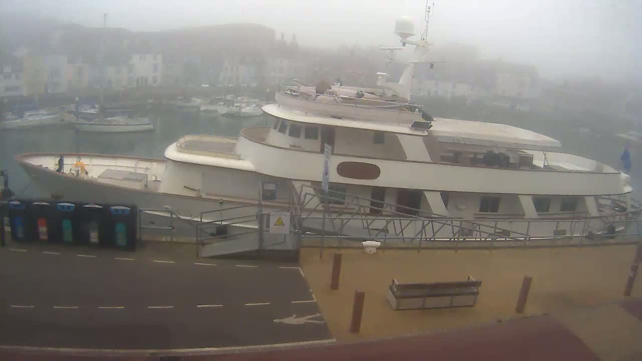 A large motor yacht is docked at a harbor in foggy conditions, with other smaller boats visible in the background.