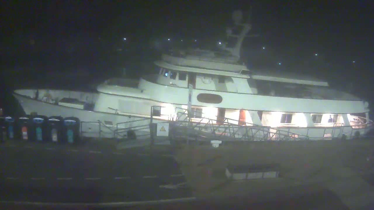 A large, white motor yacht is docked at night under dark, overcast skies.