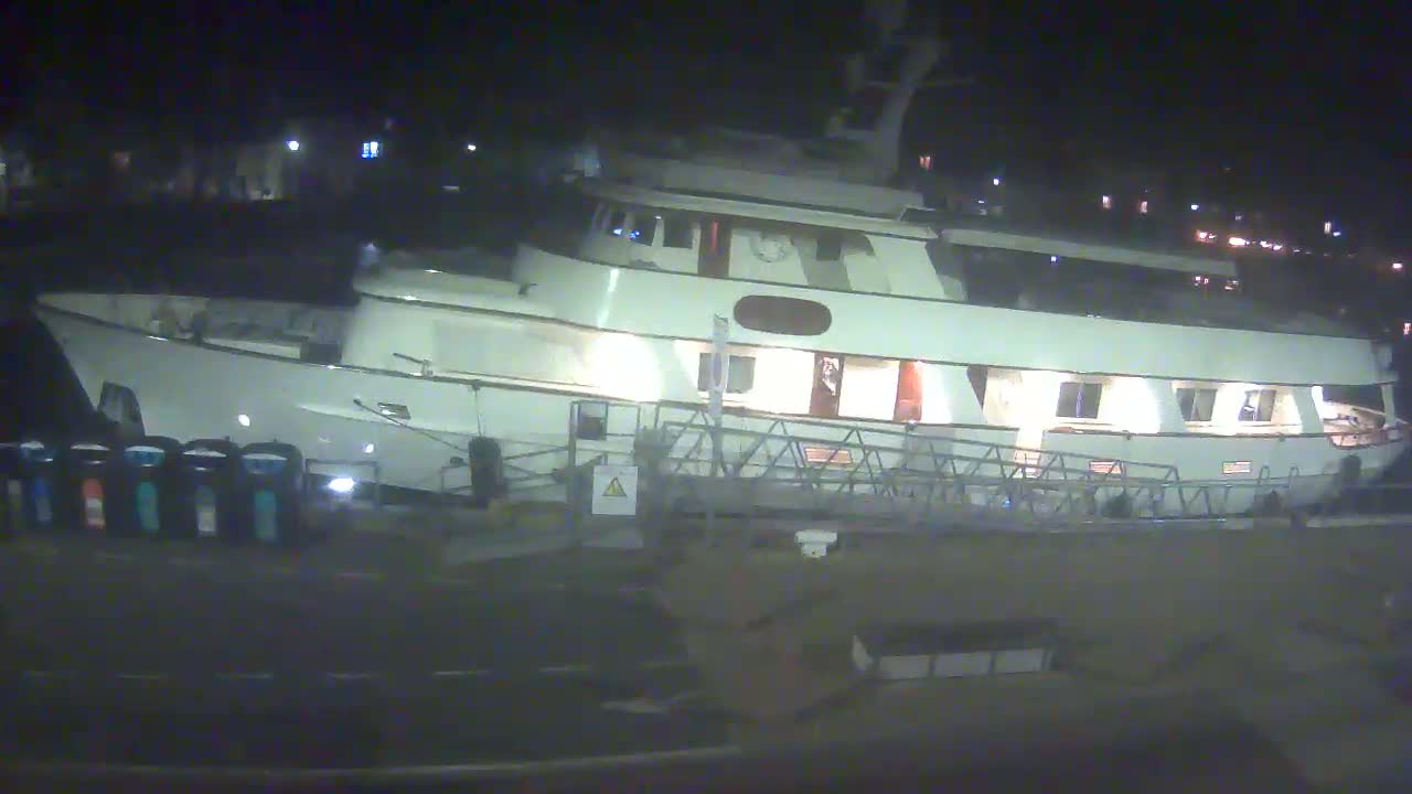 A large, white yacht is docked at night, its lights illuminated.