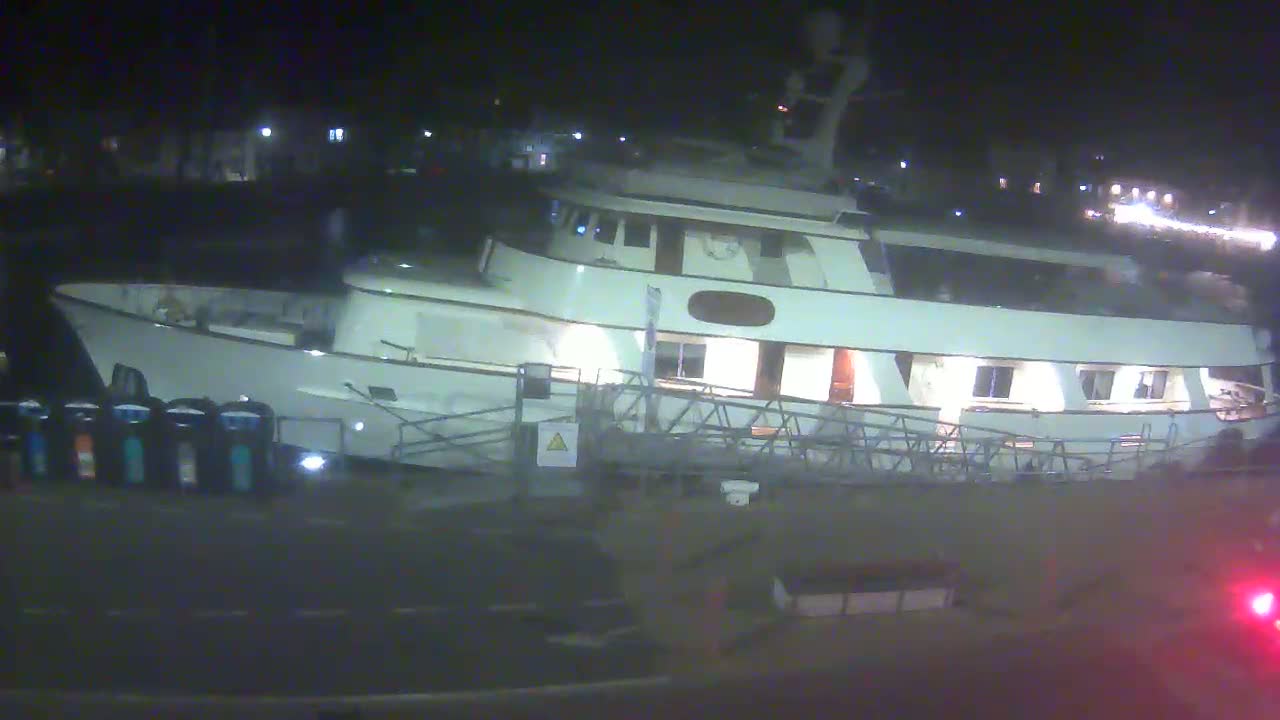 A large, white motor yacht is docked at a pier at night.