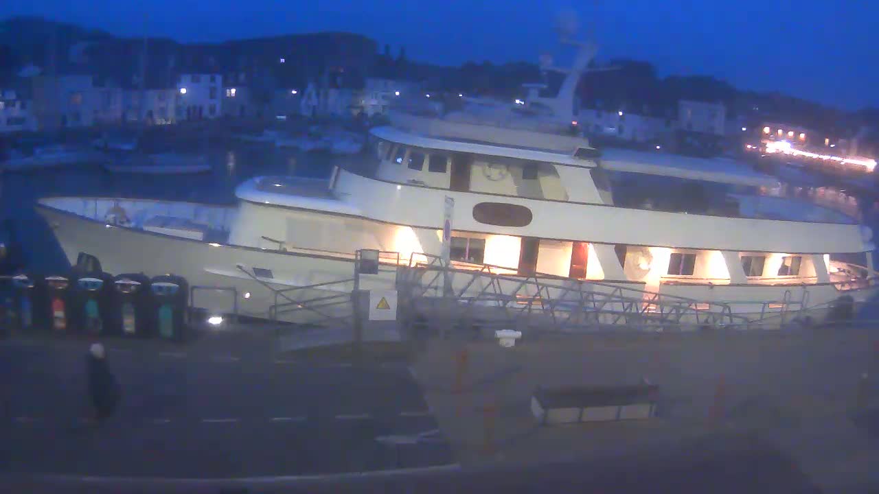 A large, white yacht is docked at a harbor at night under a dark blue sky.