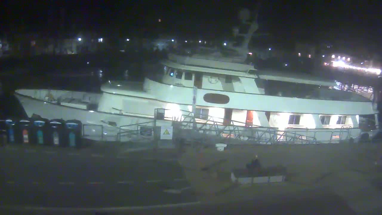 A large, white yacht is docked at night, with its interior lights on.
