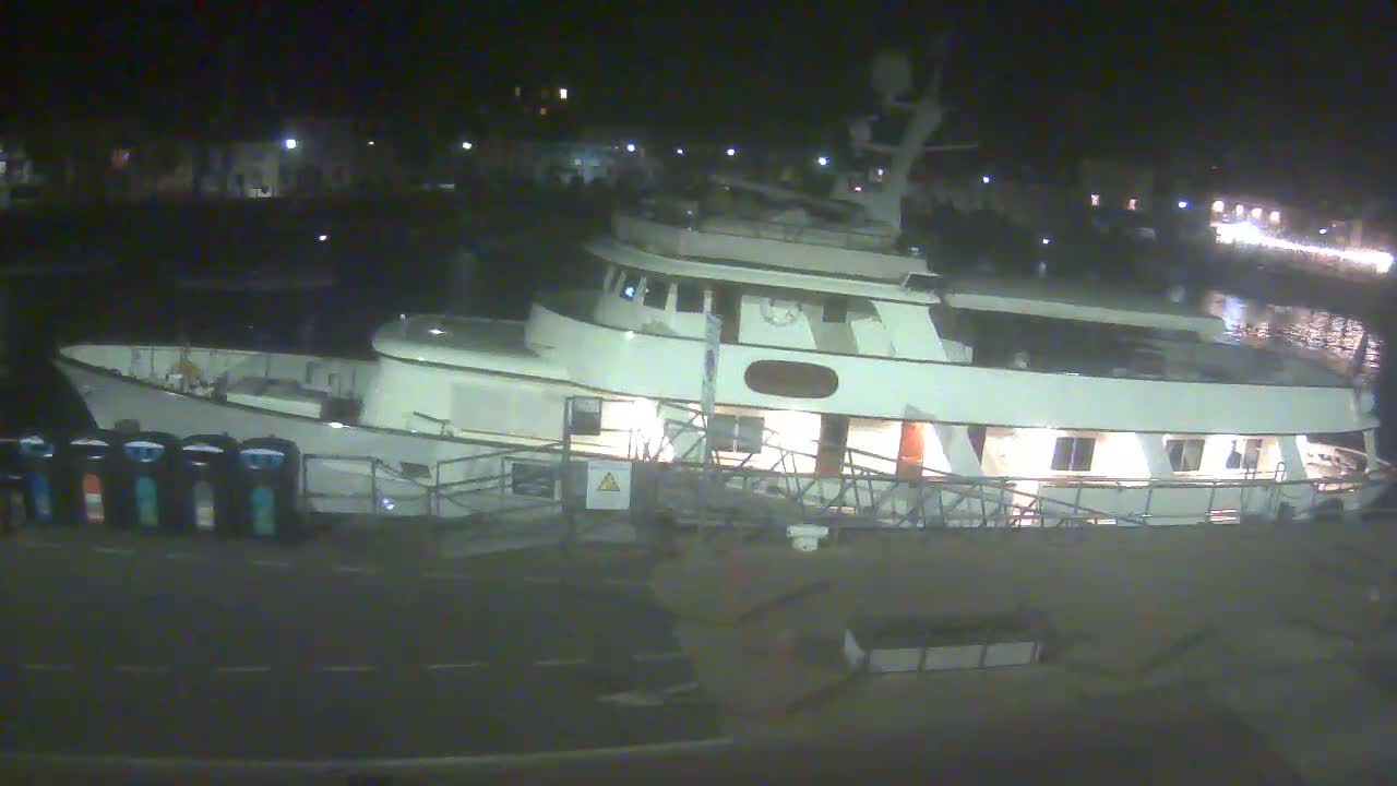 A large, white yacht is docked at a pier at night, under calm conditions.