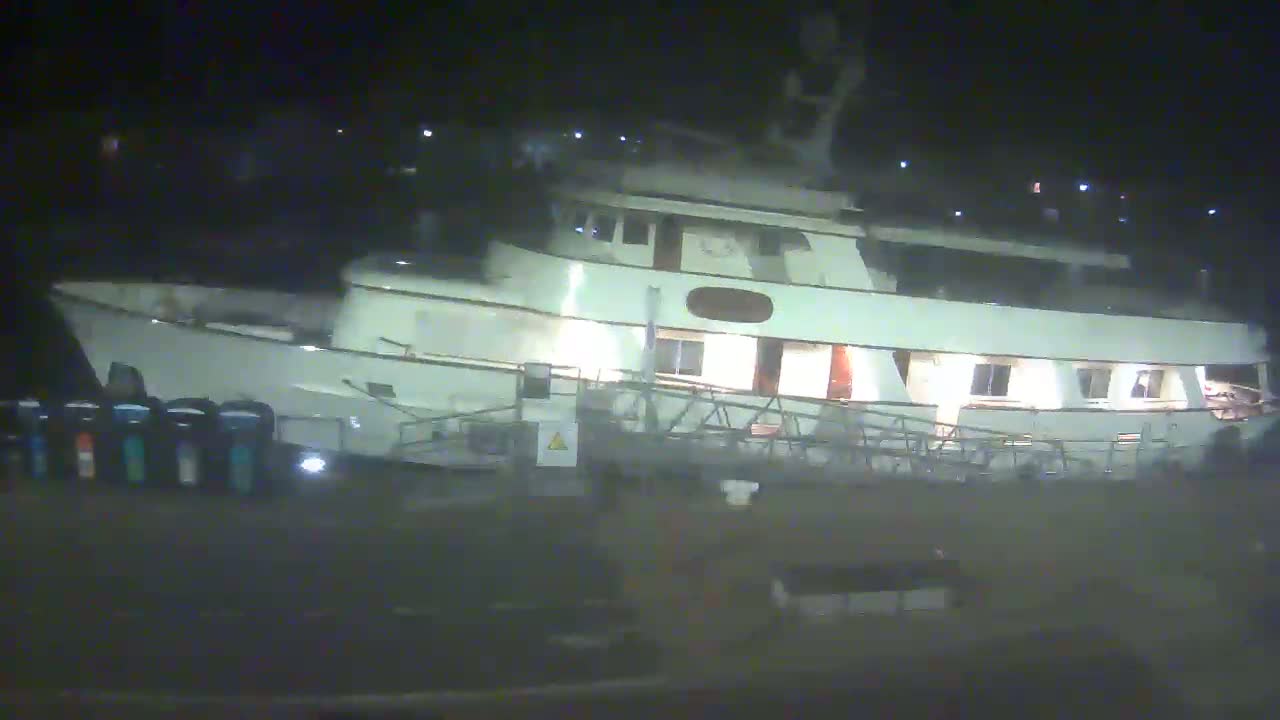 A large, light-colored yacht is docked at night, illuminated by interior lights.