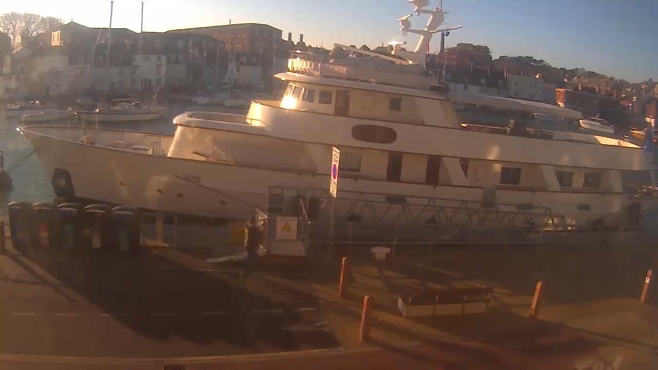 A large, light-colored motor yacht is docked at a harbor under a clear, bright sky.