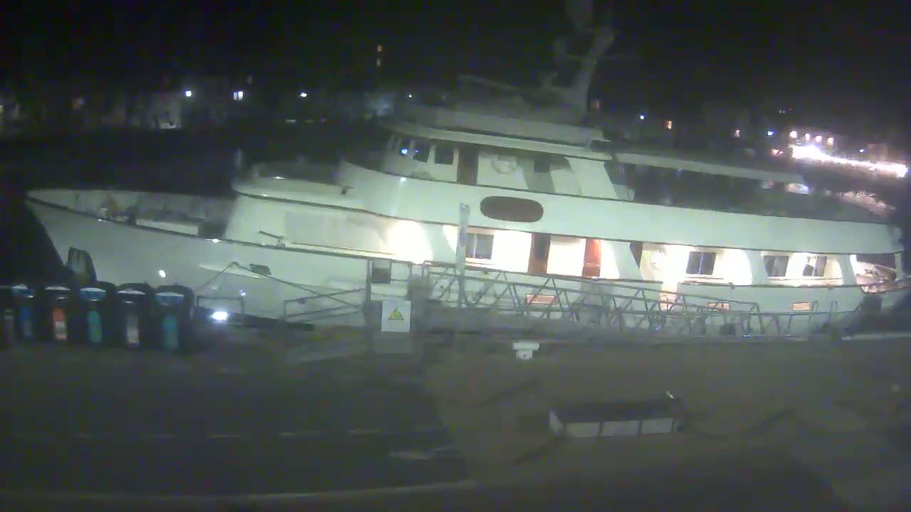 A large, white yacht is docked at night, its interior lights illuminated.