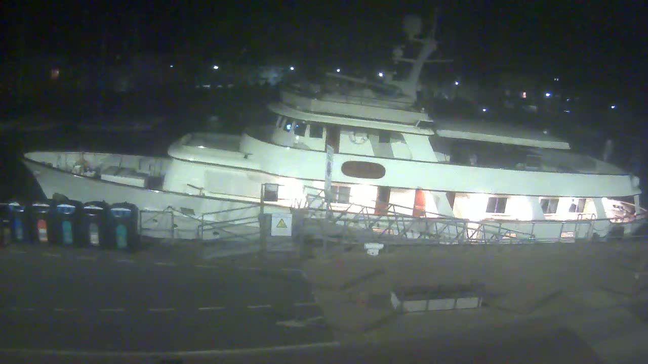 A large, white yacht is docked at night, illuminated from within.