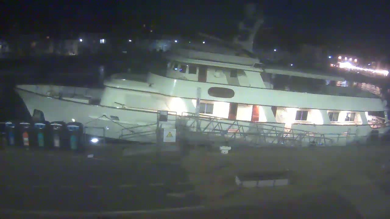 A large, white yacht is docked at night, its lights illuminated.