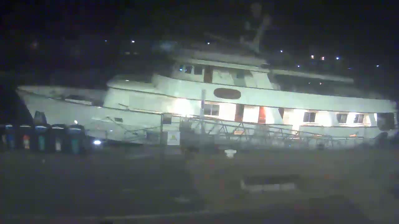 A large, light-colored motor yacht is docked at night.