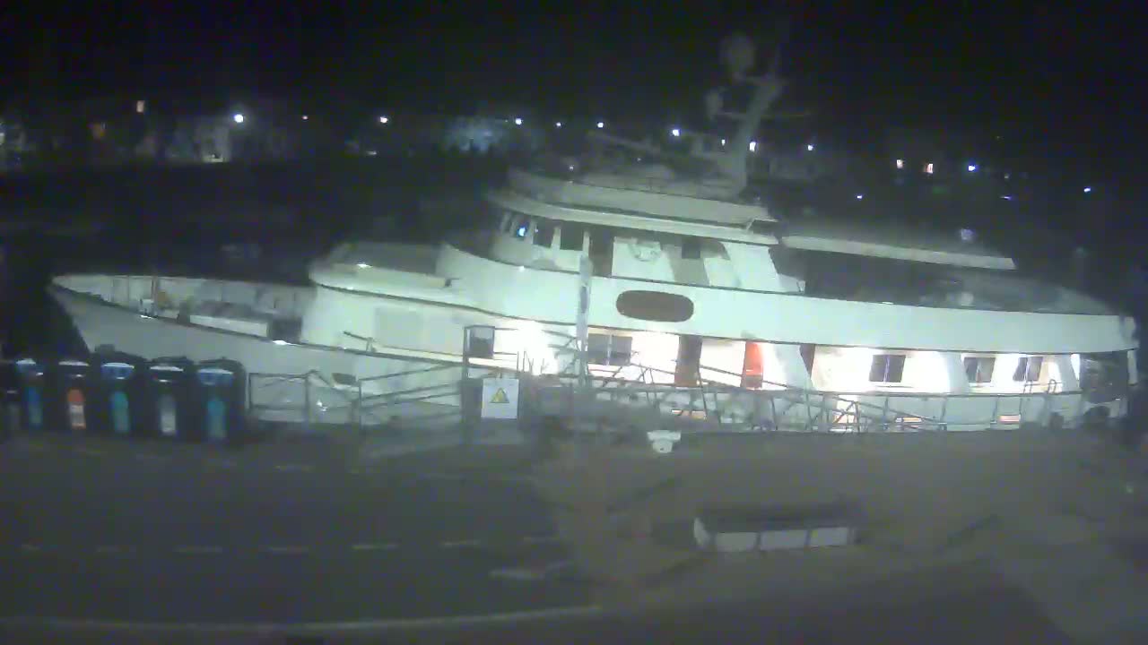 A large, light-colored yacht is docked at night under dark, clear skies.