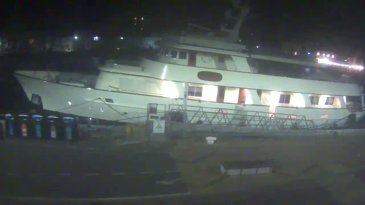A large, light-colored motor yacht is docked at night.