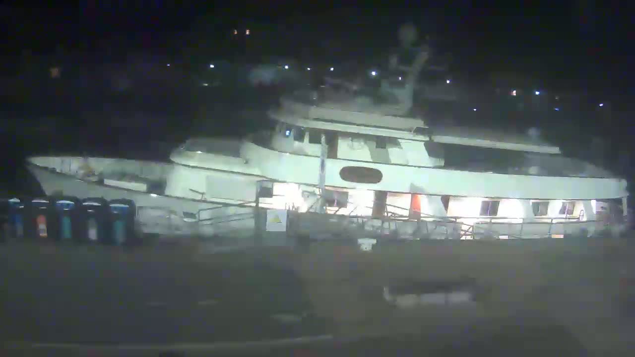 A large, light-colored motor yacht is docked at night.