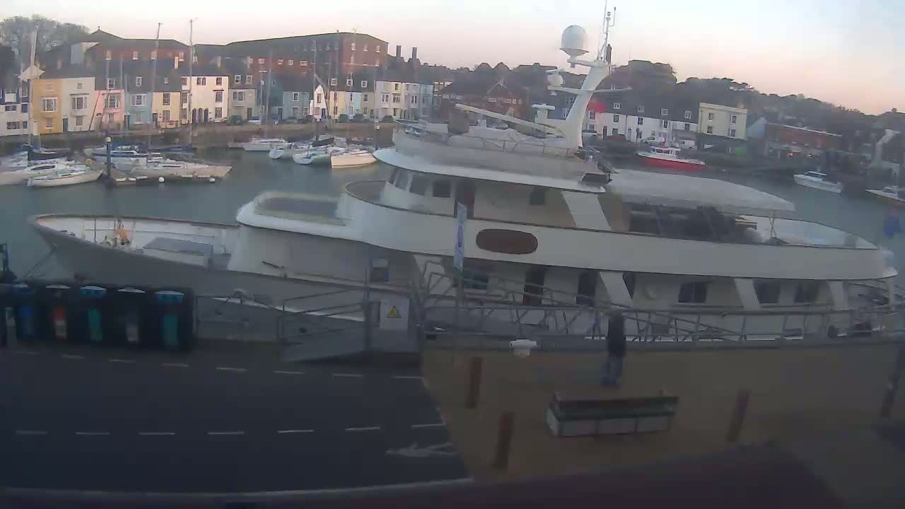 A large motor yacht is docked in a harbor filled with smaller sailboats under a twilight sky.