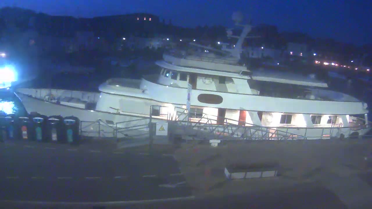 A large, white yacht is docked at night, with its lights on.