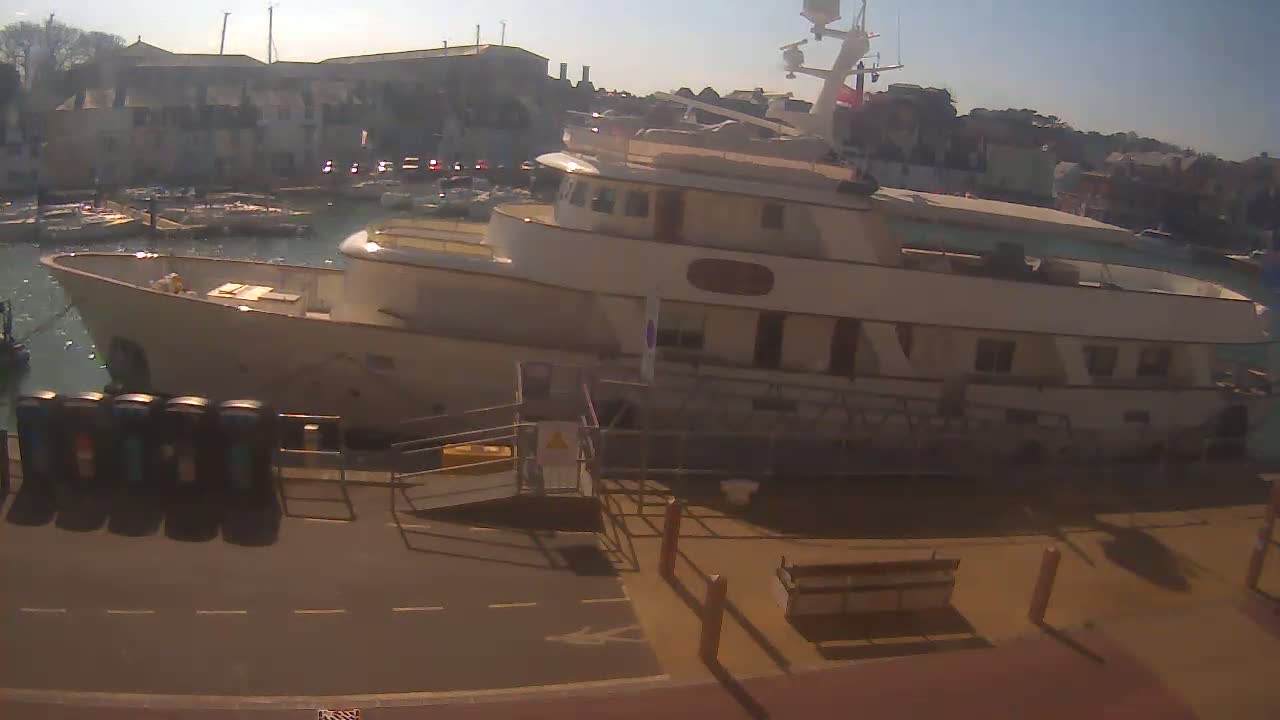 A large, light-colored yacht is docked at a marina on a sunny day.
