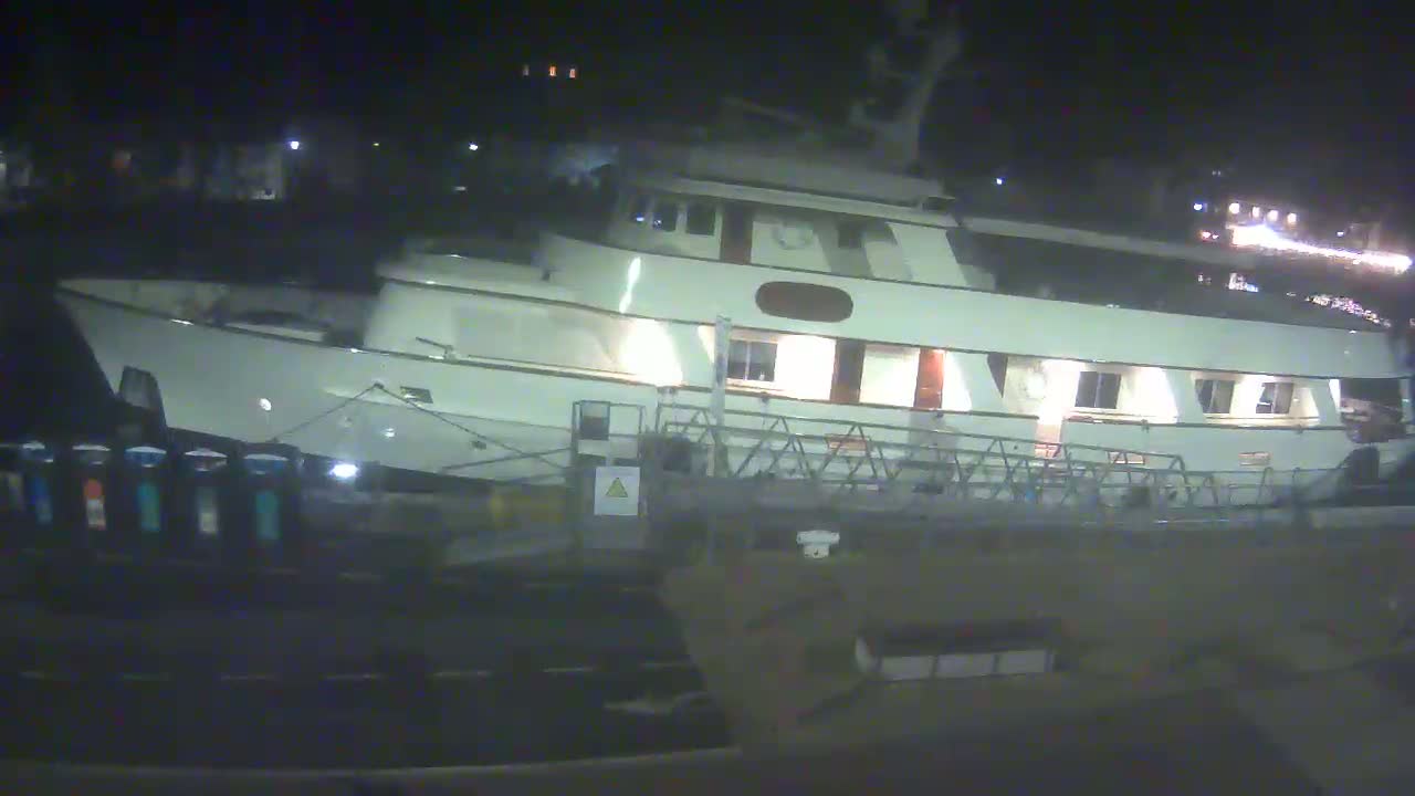 A large, white yacht is docked at night, its lights illuminated against a dark background.
