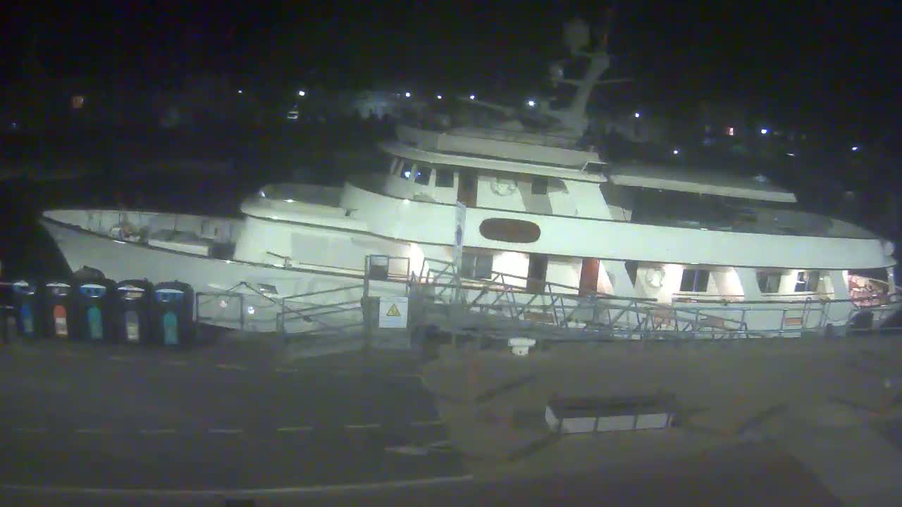 A large, white motor yacht is docked at night under dark conditions.