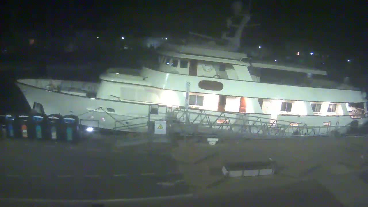 A large, white yacht is docked at night, illuminated by interior lights.