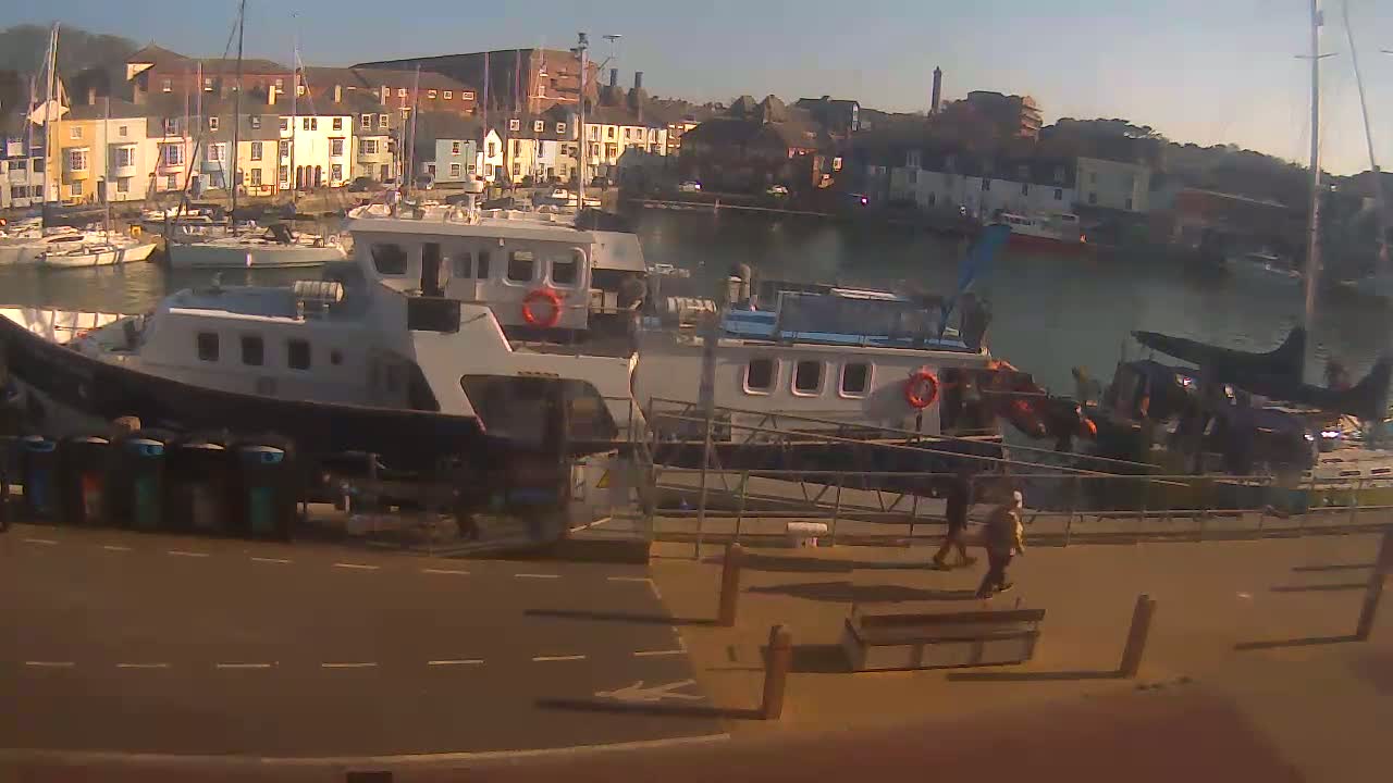 Several boats are docked at a harbor in front of a row of colorful buildings on a sunny day.