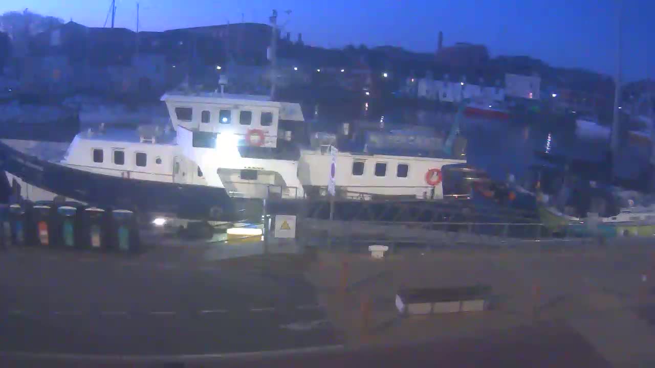Two large boats are docked at a harbor at twilight under a dark blue, clear sky.