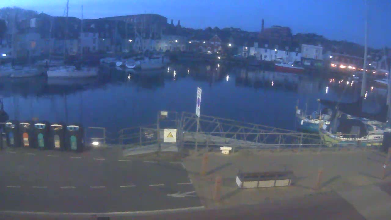 A calm harbor at twilight, filled with moored boats and overlooked by buildings along the waterfront.