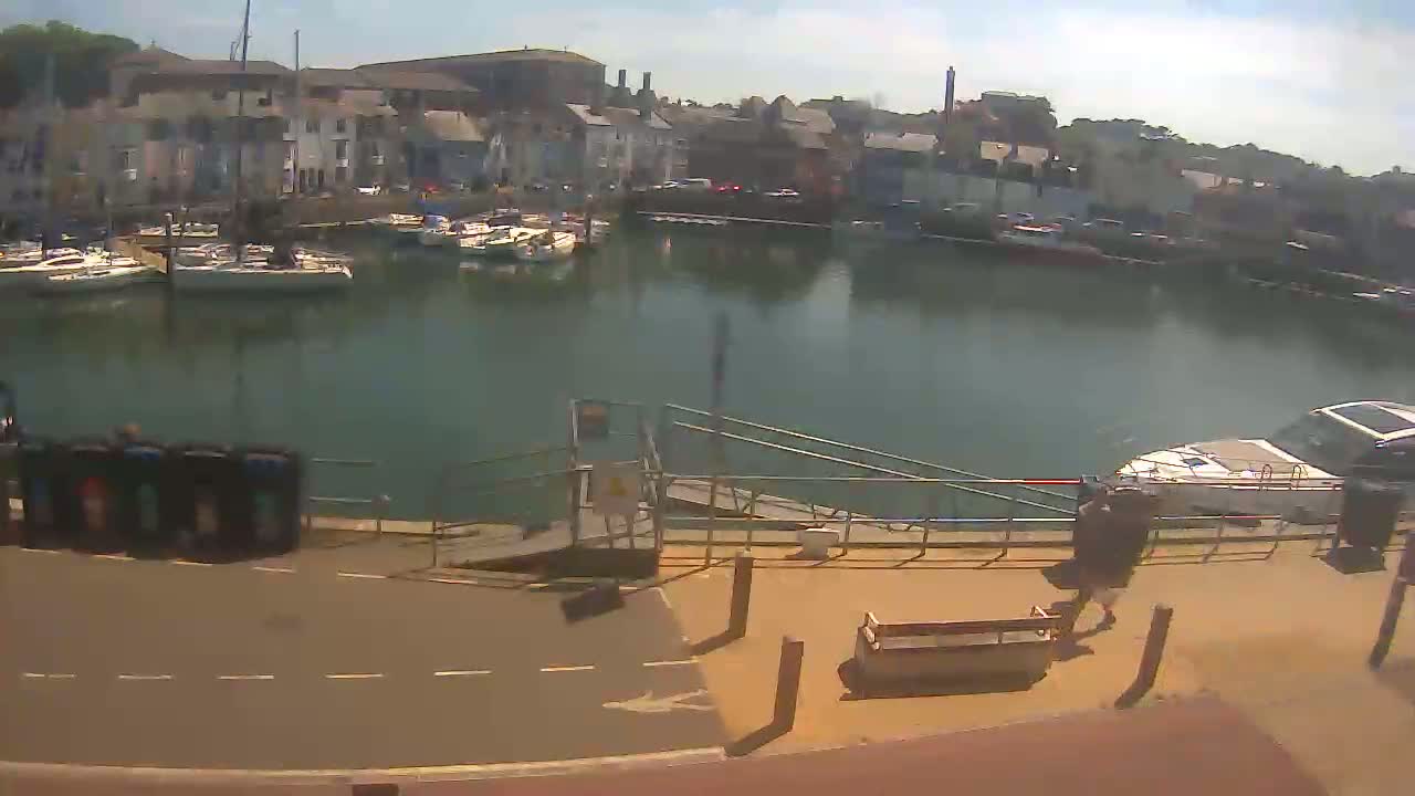 A harbor filled with sailboats and motorboats on a sunny day, with a person walking near a dock.