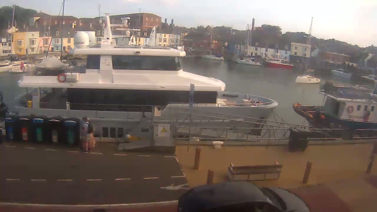 A large passenger ferry is docked at a harbor on a hazy day, with smaller boats and buildings visible in the background.