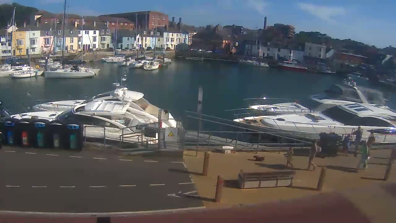 A harbor filled with numerous boats and yachts on a sunny day, with several people standing near a docked motorboat.