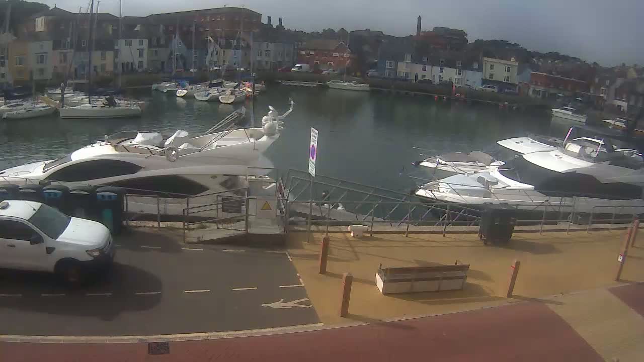Two large motor yachts are docked at a marina next to a white pickup truck, under an overcast sky.