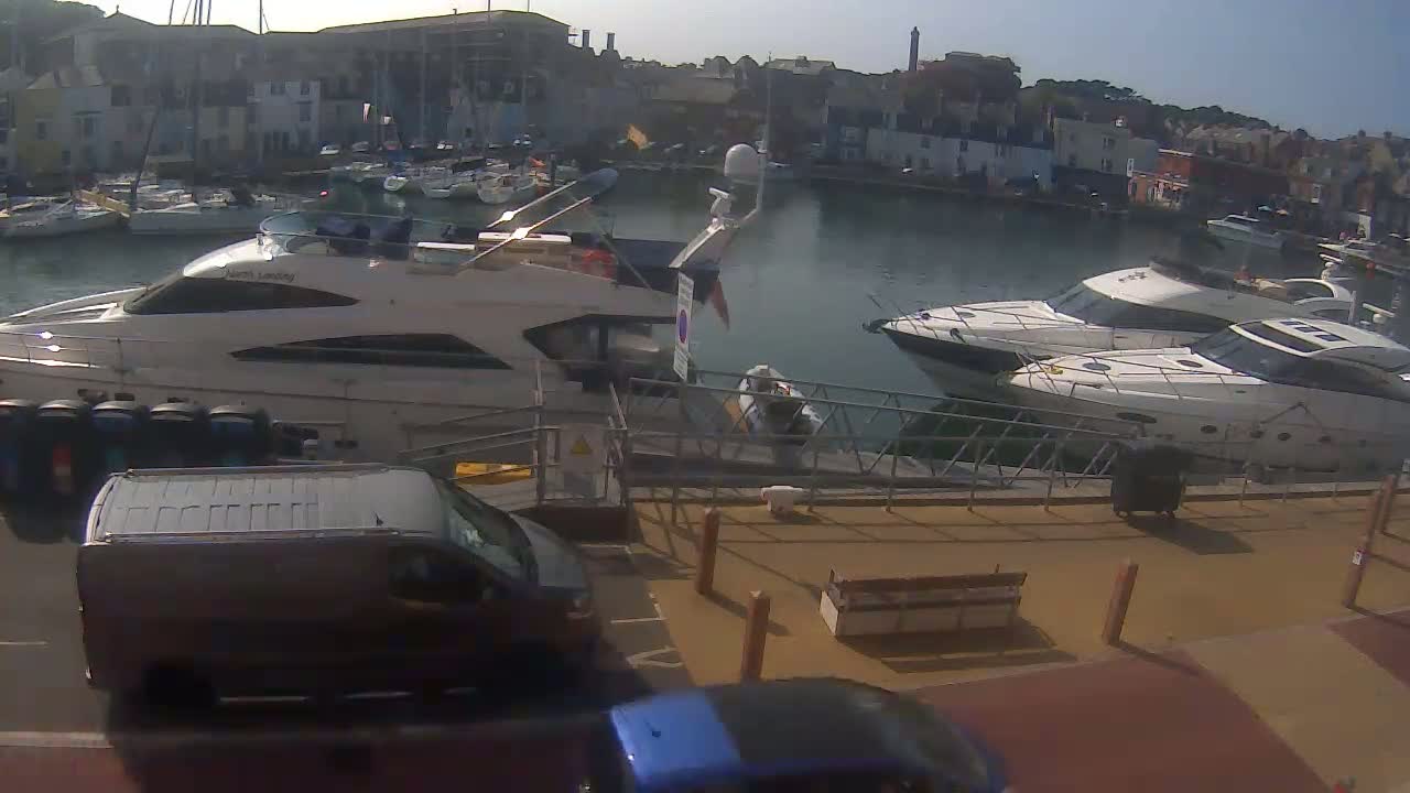 A large motorboat is docked at a harbor filled with smaller sailboats, under an overcast sky.