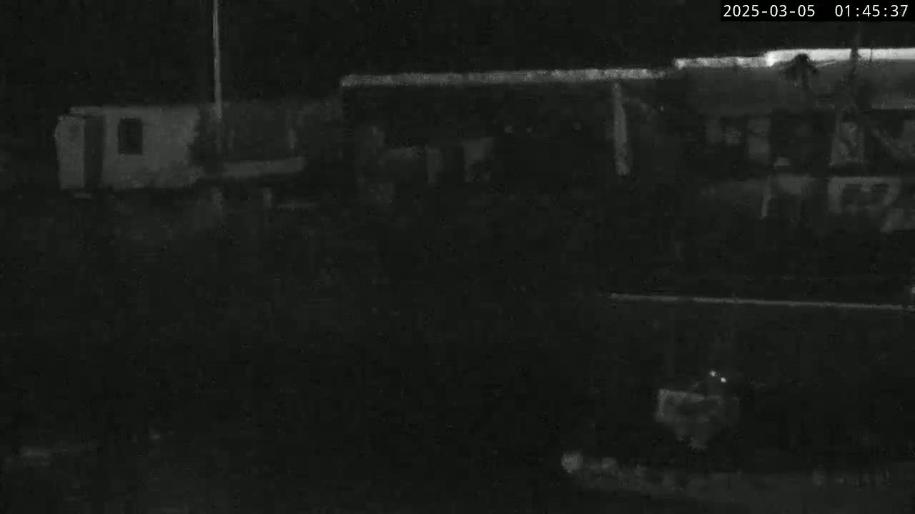A low-light, nighttime image shows several dark, indistinct structures, possibly buildings or vehicles, in an outdoor setting.